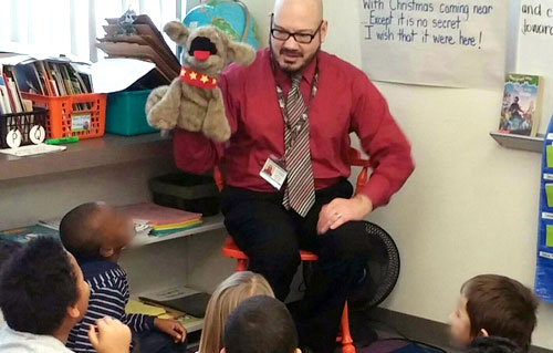 Teacher holding puppet presenting to young students